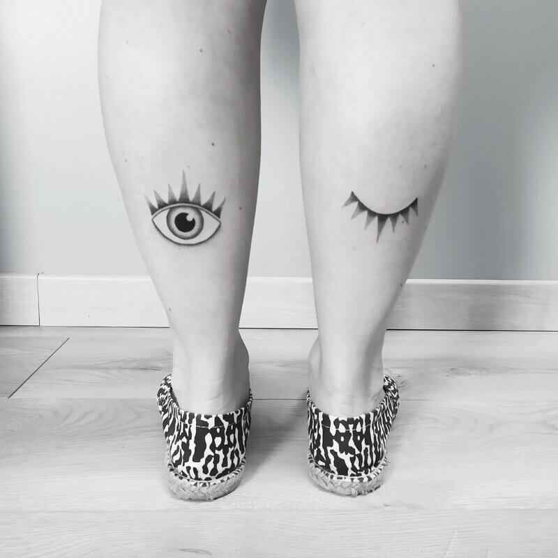 Un tatouage handpoke sur les mollets d'un oeil ouvert et d'un clin d'oeil